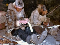 1950s Carving ivory. Kotzebue, AK. Wearing beaver skin parka with wolf ruff. Ruffon right is wolverine skin.