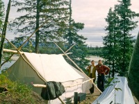 Joyce and Dan Denslow in front of white wall tent.  Ambler River in the background, small wood stove beside the tent.
